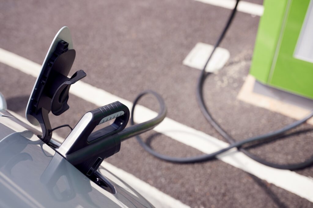 Close Up Of Power Cable Charging Electric Car Outdoors In Supermarket Car Park