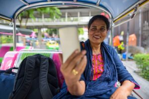 Mature Indian woman sitting in tuk tuk and using mobile phone